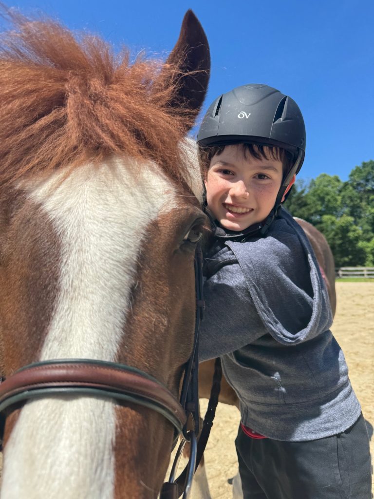 A boy smiles at the camera as he hugs a brown and white horse on the neck.