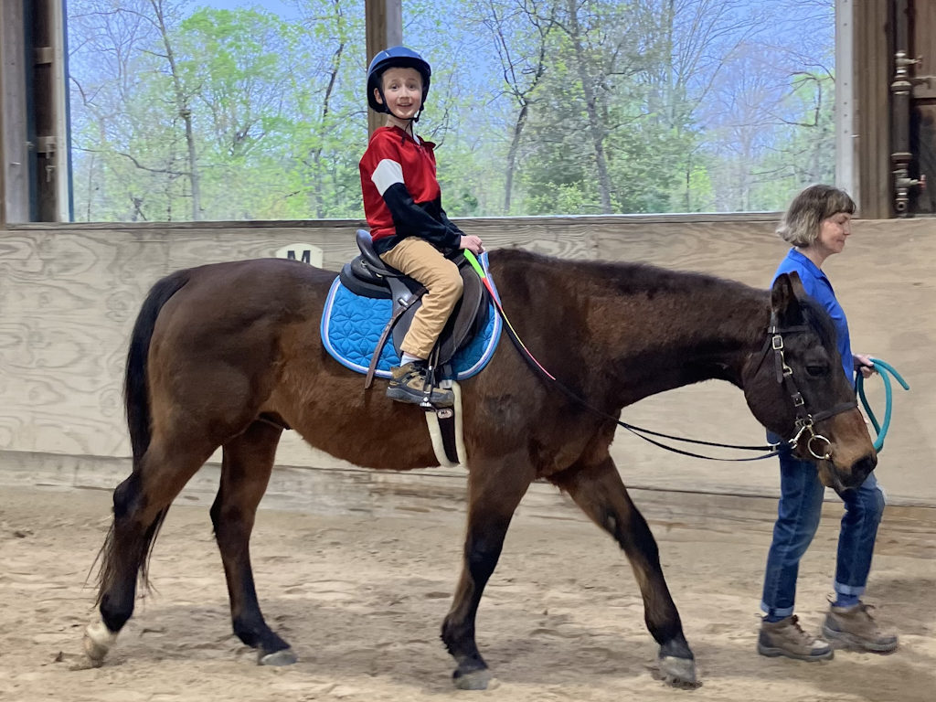 Tattoo calmly walks alongside a leader along the side of the arena while the boy riding him grins at the camera.